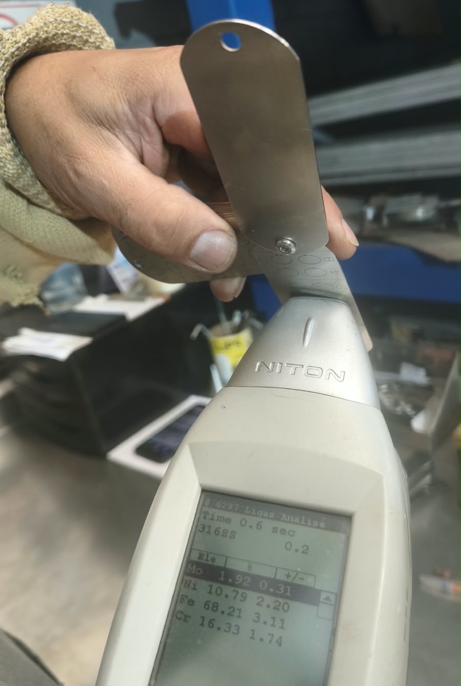 Espectrômetro de raios X encostado numa placa INOXKEY, com a tela mostrando liga 316 e 1,92% de molibdênio